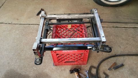 1991 Ford Festiva - A car seat frame is elevated on milk crates, with tools visible on the concrete floor.