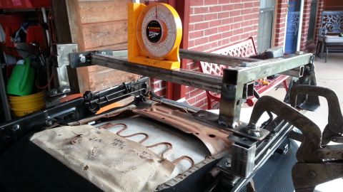 1991 Ford Festiva - A car seat frame is mounted on a metal jig with a yellow protractor attached to measure angles.