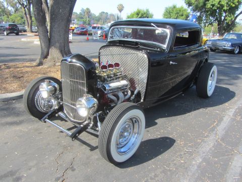 1964 Ford Ranchero - A modified black hot rod with a prominent V8 engine sits parked outdoors.