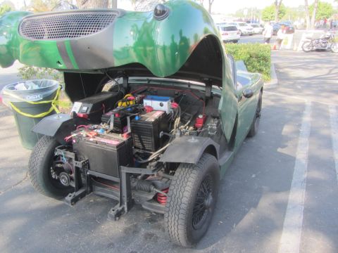 1964 Ford Ranchero - Open hood of a green sports car displays its battery setup and engine bay components.