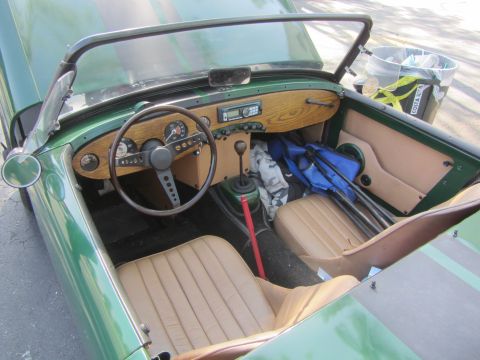 1964 Ford Ranchero - The interior of a green convertible shows tan seats, a wood-grain dashboard, and a radio, with golf clubs in the passenger seat.