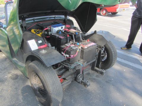 1964 Ford Ranchero - The open hood reveals a complex battery system within this green vehicle, with another red vehicle visible in the background.