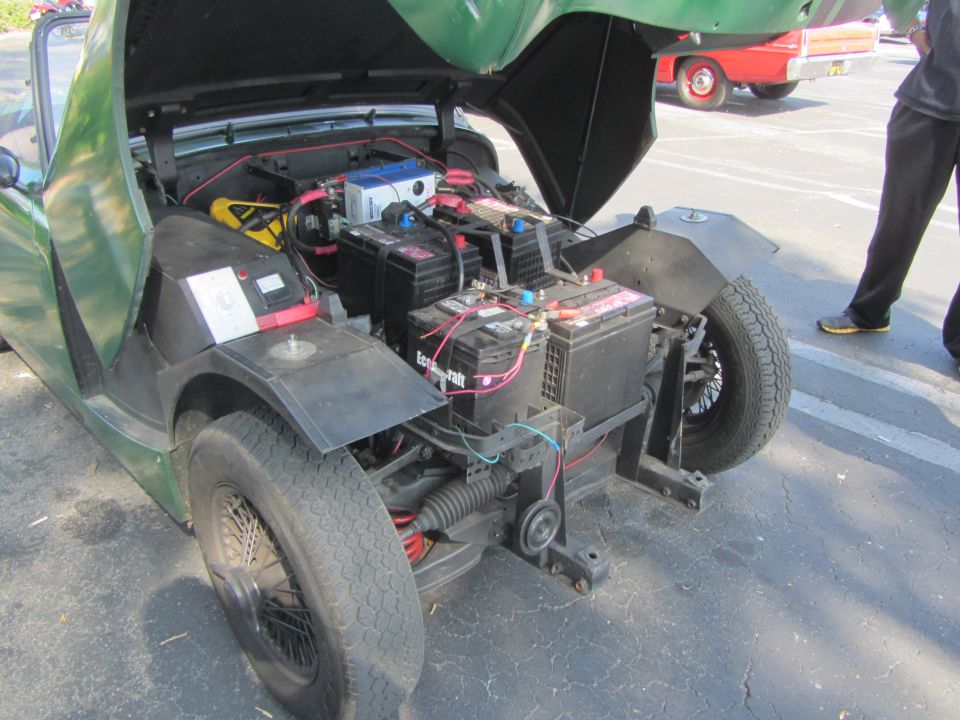 Green car's engine bay filled with multiple batteries and wiring