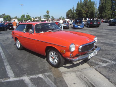 1964 Ford Ranchero - An orange Volvo P1800ES station wagon is parked at an outdoor car show with other vehicles in the background.