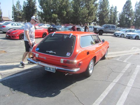 1964 Ford Ranchero - An orange Volvo P1800 ES wagon is seen from the rear in a parking lot with other vehicles present.