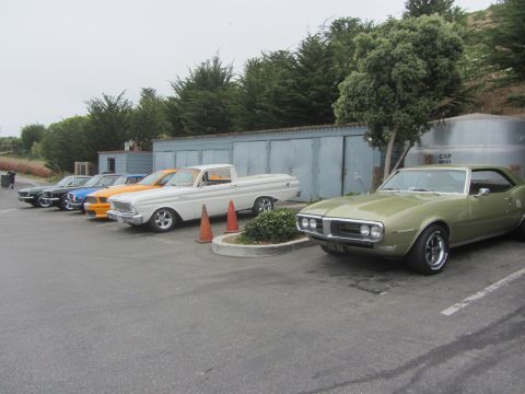 1964 Ford Ranchero - Several classic cars are parked in a lot, including a green 1967 Firebird and a white Ford Ranchero.