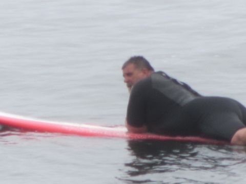 1964 Ford Ranchero - A man in a wetsuit rests on a red surfboard while floating in the water.