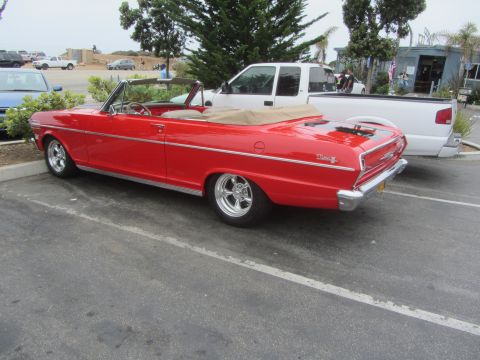 1964 Ford Ranchero - A red convertible with a tan top is parked in a lot next to a white pickup truck.