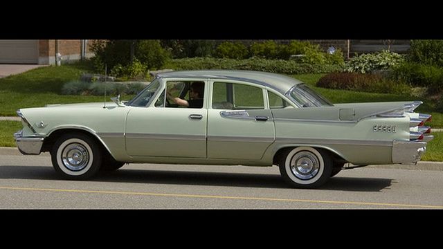Two-tone green 1959 Dodge Custom Royal sedan driving on a road, seen from the side