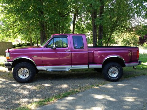1992 Ford F-150 - Side view of a lifted magenta Ford F-150 extended-cab 4x4 pickup with chrome wheels, parked on a gravel drive.