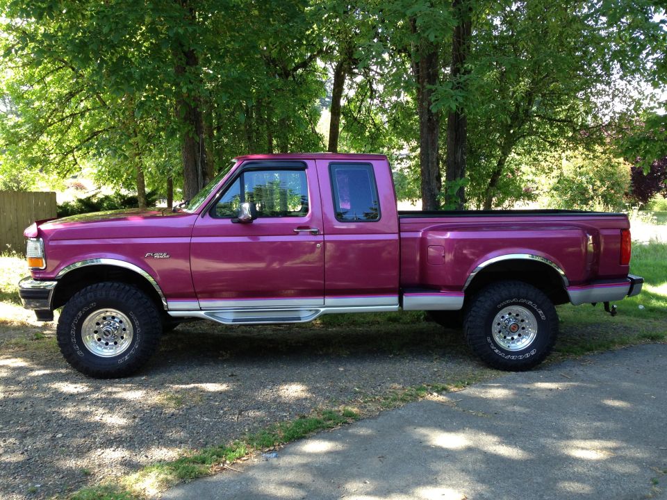 Magenta 1990s Ford F-150 extended-cab lifted 4x4 pickup parked by trees