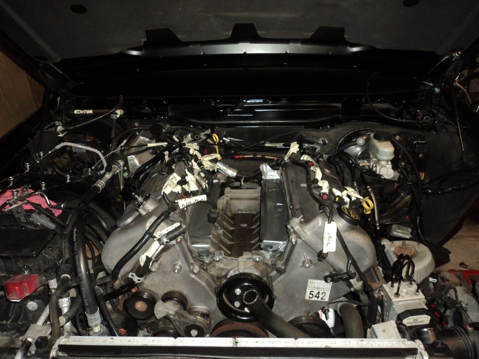 Engine bay with wiring harnesses and engine parts visible. A tag with '542' is on the engine