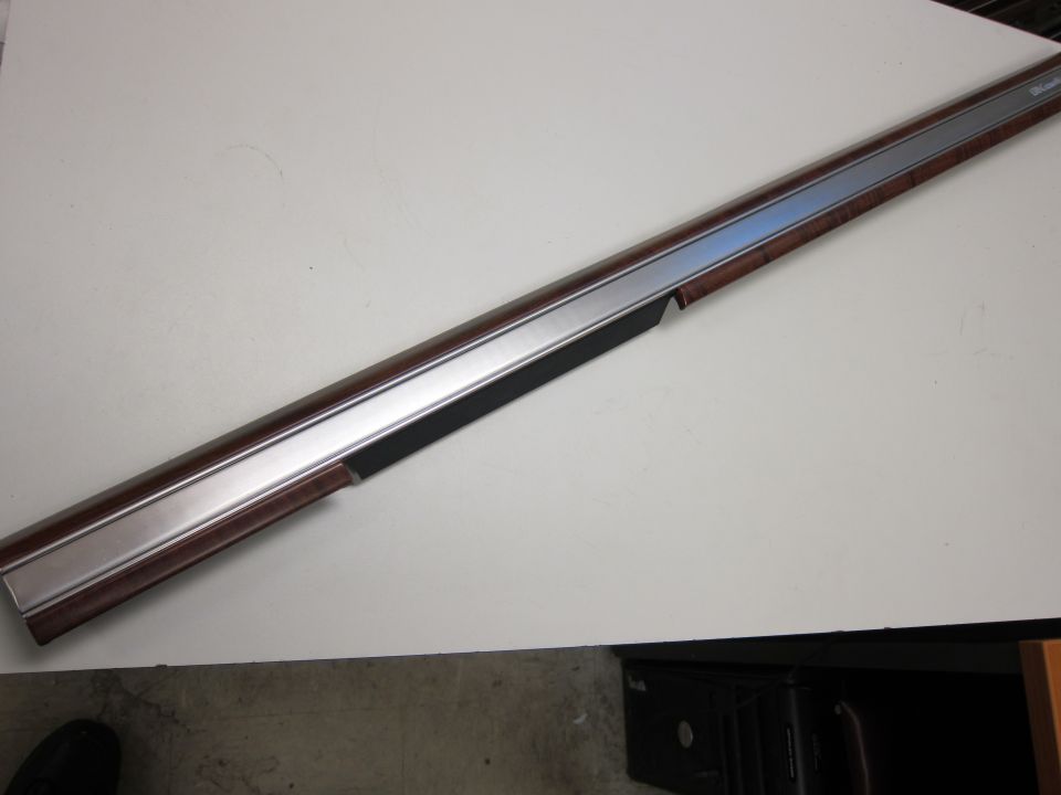 Car trim piece with wood grain and chrome accents. Text on trim reads 'Woodward'