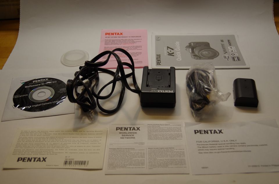 Pentax K-7 camera accessories including a CD, battery charger, battery, and manuals