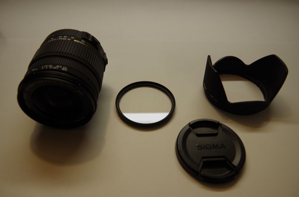 Camera lens, filter, lens hood, and lens cap laid out on a surface. The lens cap has 'SIGMA' on it