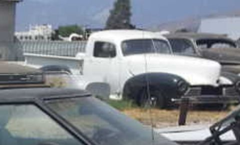 1973 Ford Ranchero - A white pickup truck with a distinctive grille and rounded fenders is parked in a lot with other vehicles.