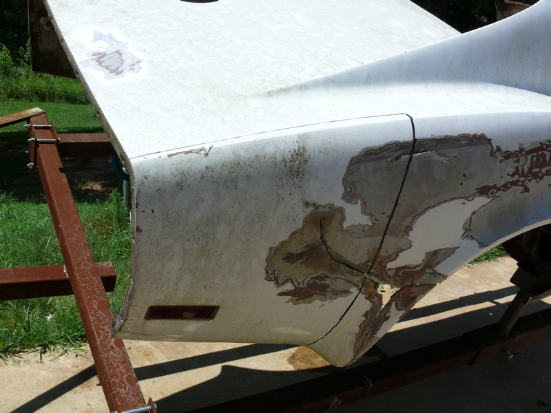 White car body panel, possibly a fender or hood, mounted on a metal stand. Paint is chipped and rusted in areas