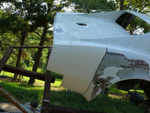 1976 Chevrolet Corvette - Car body panel undergoing restoration, mounted on a stand in a grassy area with trees.