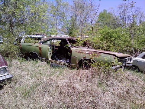 1974 Dodge Challenger - This heavily rusted 1970s muscle car sits abandoned in a junkyard, surrounded by weeds and other vehicles.