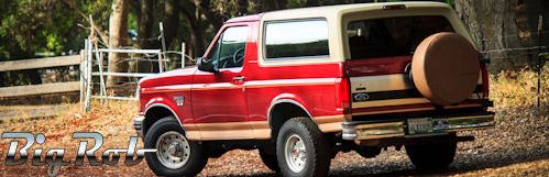 Red and tan Ford Bronco parked on a dirt road with a spare tire on the back