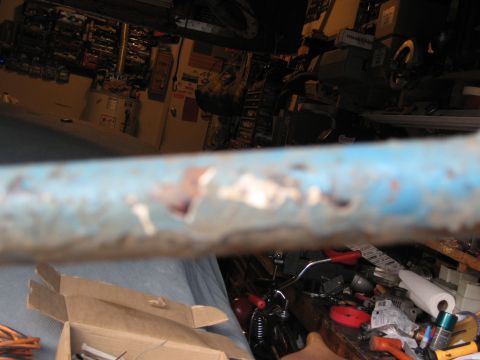 1994 Ford Bronco - A close-up of a rusty blue metal bar obscures a cluttered garage scene with tools and shelves.