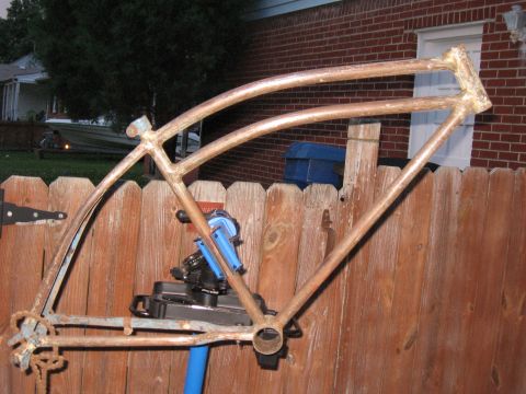 1994 Ford Bronco - A weathered bicycle frame, showing signs of rust and previous paint, is mounted on a repair stand in front of a wooden fence.