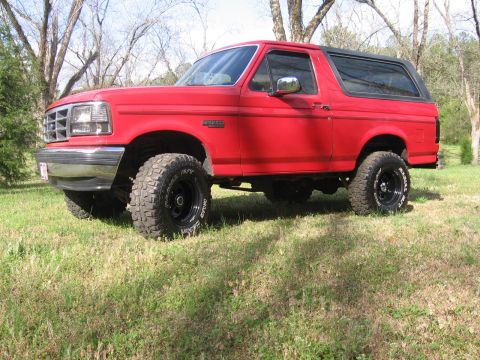 1992 Ford Bronco - A red 1992 Ford Bronco with a lifted suspension and aggressive off-road tires sits on a grassy field.