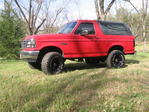 1992 Ford Bronco - This red 1992 Ford Bronco is parked on a grassy field with trees in the background.