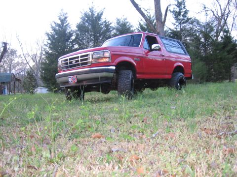 1992 Ford Bronco - A red 1992 Ford Bronco sits in a grassy field with trees in the background.