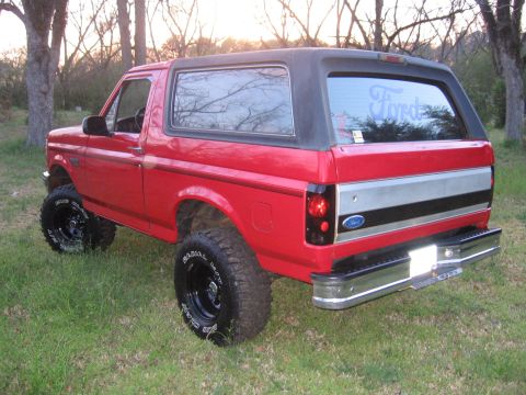 1992 Ford Bronco - This red 1992 Ford Bronco features a black removable top and lifted suspension, seen here in a three-quarter front view.