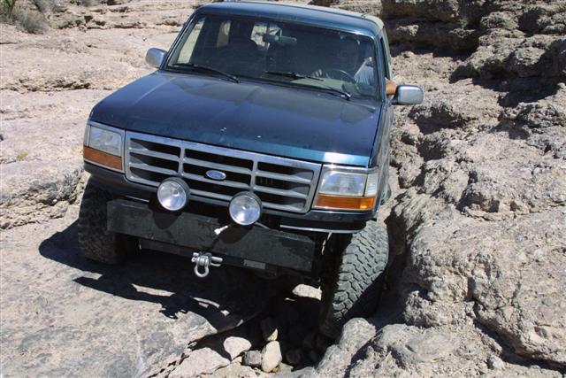 Dark green Ford Bronco with winch bumper and driving lights crawling over desert rocks