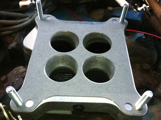 Close-up of a four-barrel carburetor spacer with mounting studs