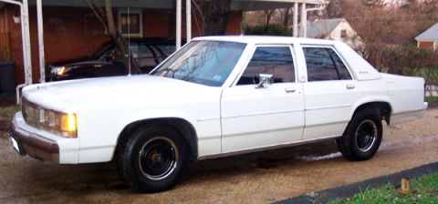 1991 Ford Crown Victoria LTD - A white sedan is parked outside a house, with a second vehicle visible in the background.