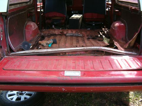 1979 Ford Bronco - The interior of a red SUV shows significant rust damage on the floor and worn seats, with a metal bar across the cargo area.