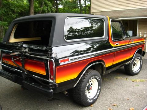 1994 Ford Bronco - This classic Ford Bronco features a distinctive sunset-themed stripe and a rear-mounted spare tire carrier.