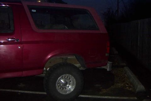 1994 Ford Bronco - Rear side view of a red 1994 Ford Bronco parked outdoors after dark.