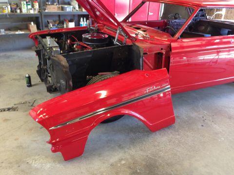1964 Ford Fairlane - A detached red fender with "Fairlane 500" script sits in front of the exposed engine bay of a classic car.