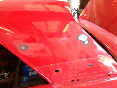 1964 Ford Fairlane - Close-up of a red car hood showing areas prepped for repair, with visible body filler and mounting holes.