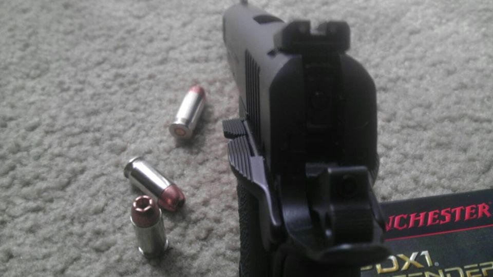 Black pistol with three bullets on carpet, Winchester box visible