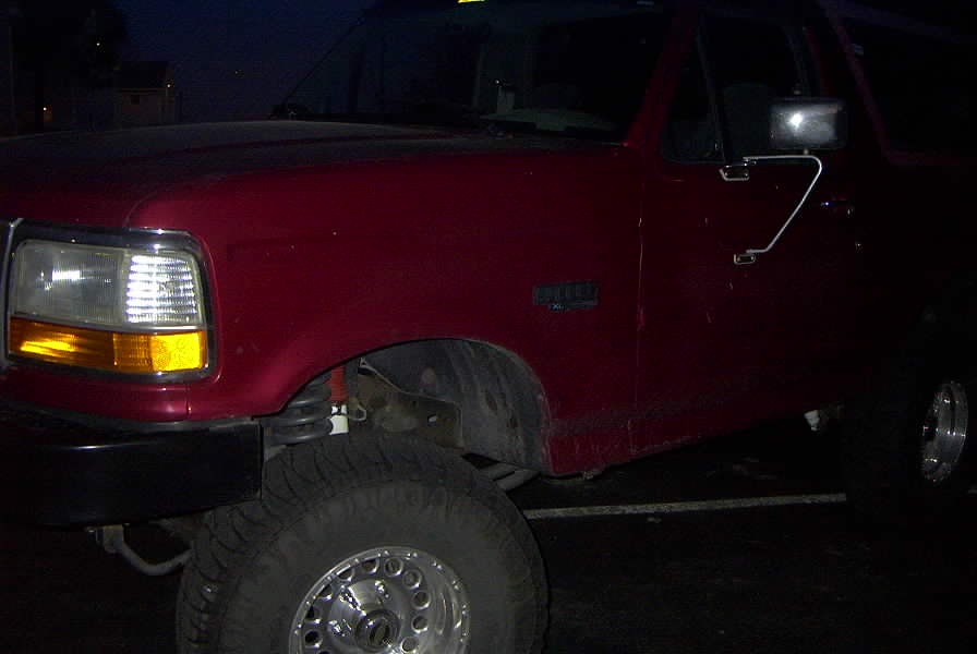 Red Ford Bronco, front 3/4 view, showing headlights, fender, and wheel