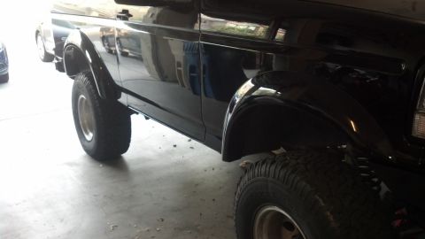1995 Ford Bronco - The side profile of a black SUV is visible, parked indoors with reflections on its glossy paint.