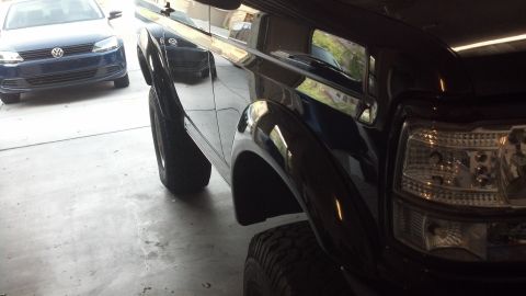 1995 Ford Bronco - Close-up of a black SUV's front fender and headlight, with a blue sedan visible behind it.