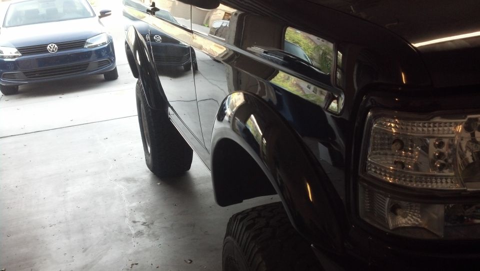 Black SUV fender, headlight, and tire. Blue Volkswagen sedan in background