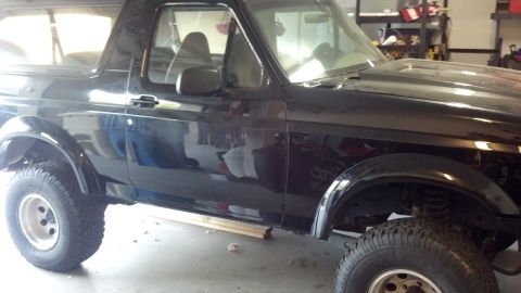 1995 Ford Bronco - The side profile of a black SUV is visible, parked indoors with its tires and suspension components exposed.