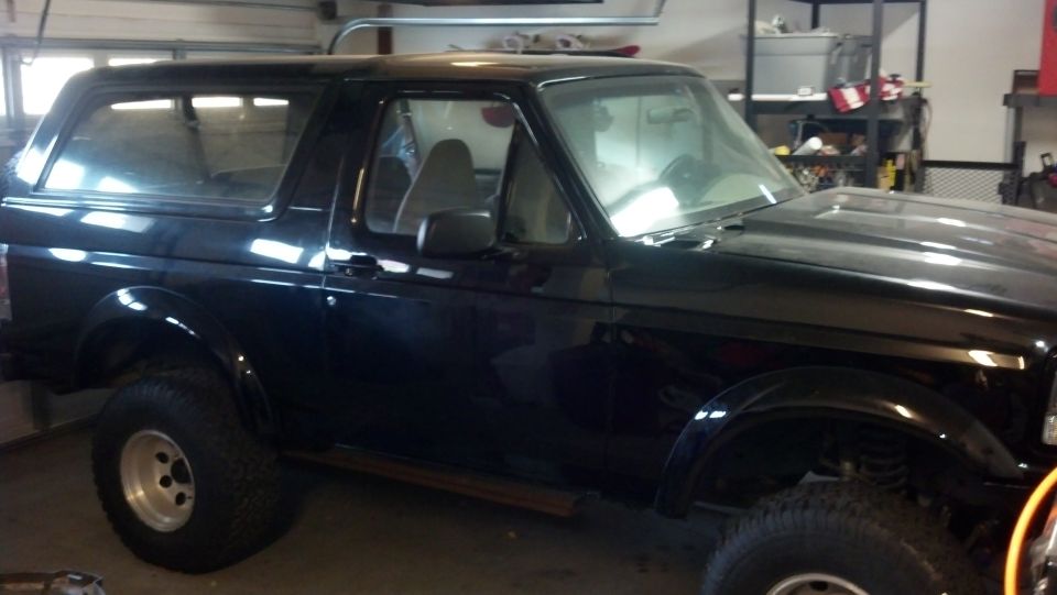 Black SUV with aftermarket wheels and side steps, parked indoors