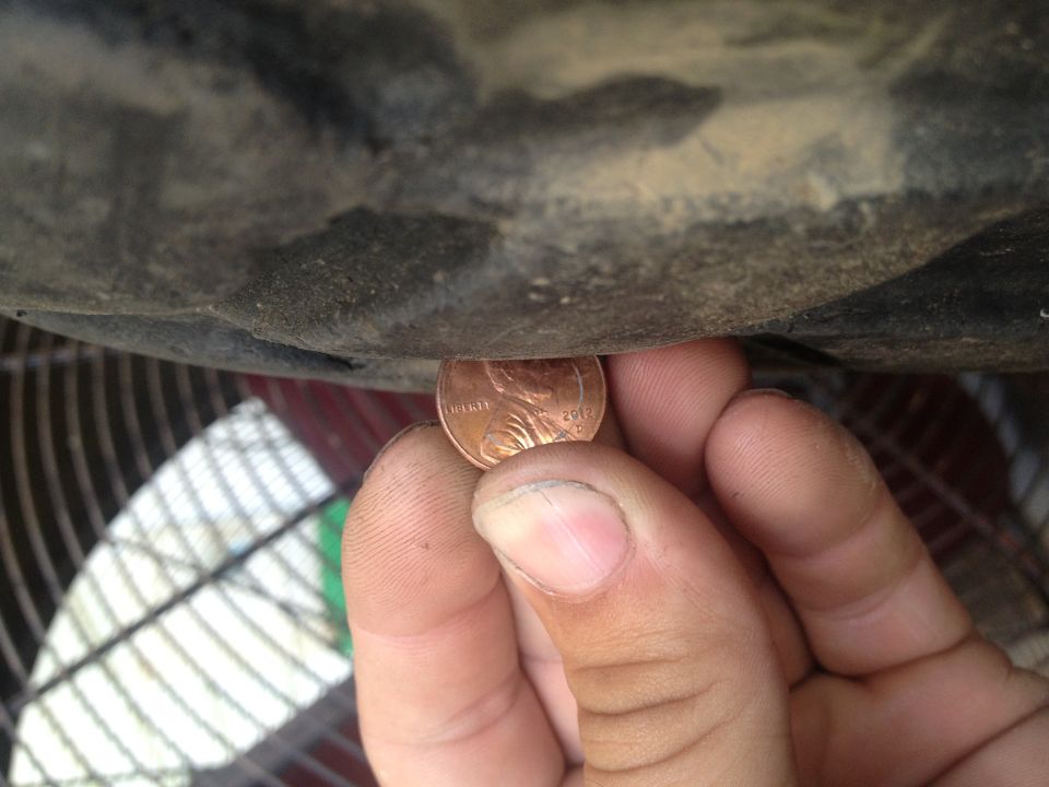 Penny held under dark, dirty vehicle undercarriage, with a fan visible below