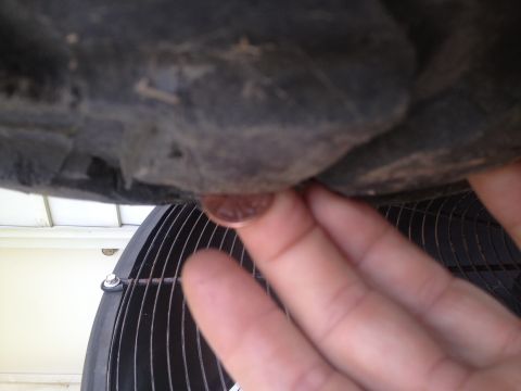 2000 Jeep Wrangler - A penny is held near the edge of a large fan grill, with a dark, textured surface above.