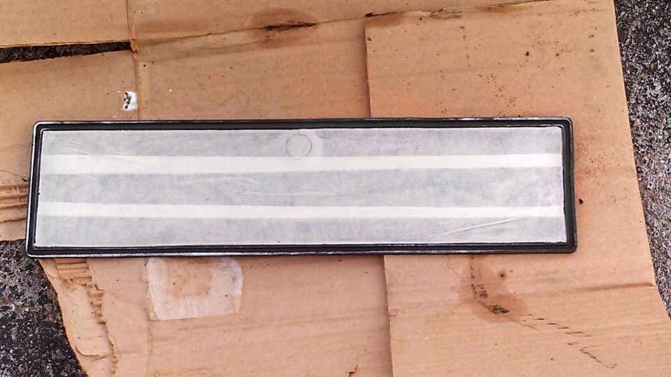 Rectangular chrome trim piece with white stripes on a piece of cardboard