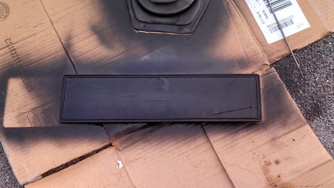 1979 Ford Bronco - A black trim piece is being spray-painted on a piece of cardboard.