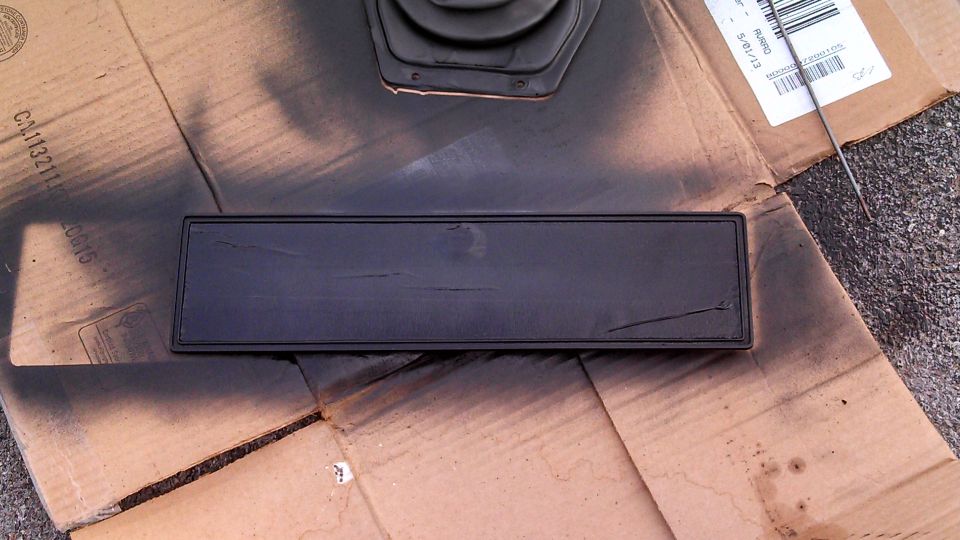 Black rectangular trim piece with cracks, resting on spray-painted cardboard
